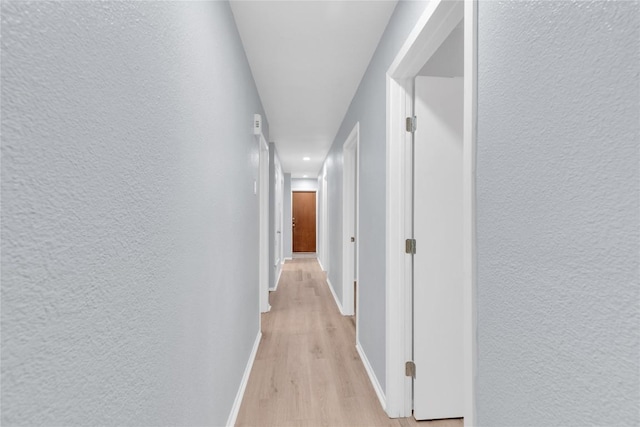 corridor featuring a textured wall, light wood-style flooring, and baseboards