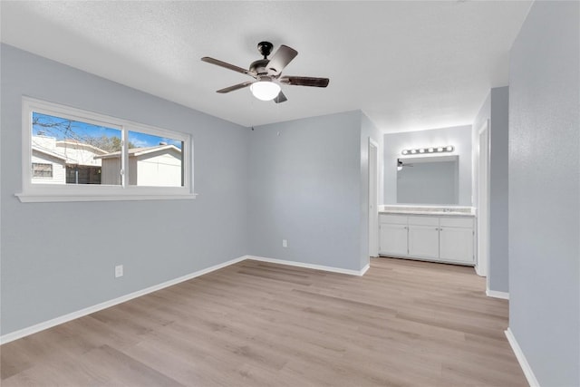 unfurnished bedroom featuring light wood-type flooring, ensuite bath, baseboards, and ceiling fan