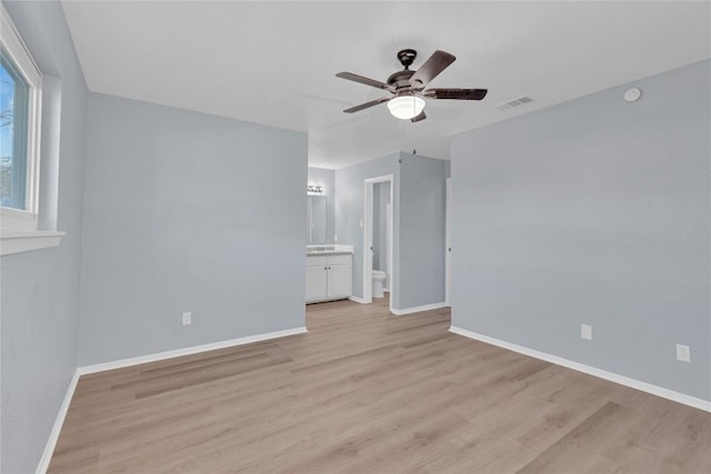 unfurnished bedroom with ensuite bathroom, a ceiling fan, visible vents, baseboards, and light wood finished floors