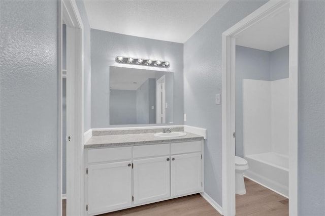 bathroom with a textured wall, toilet, wood finished floors, vanity, and baseboards