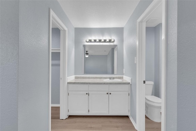 bathroom with a textured wall, toilet, wood finished floors, vanity, and baseboards