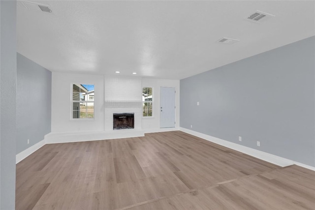 unfurnished living room with a brick fireplace, light wood-style flooring, visible vents, and baseboards