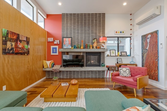 living area featuring an AC wall unit, a tiled fireplace, wood finished floors, and recessed lighting