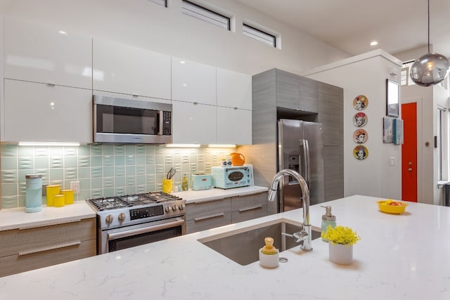 kitchen featuring light stone counters, stainless steel appliances, a sink, decorative backsplash, and modern cabinets