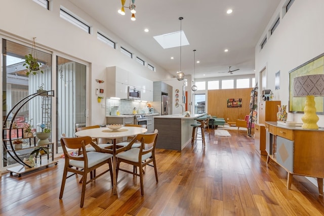 dining space featuring hardwood / wood-style floors, a skylight, a high ceiling, and recessed lighting