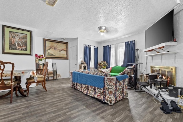 living room with a brick fireplace, a textured ceiling, visible vents, and wood finished floors