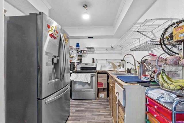 kitchen with crown molding, stainless steel appliances, a sink, a textured ceiling, and wood finished floors