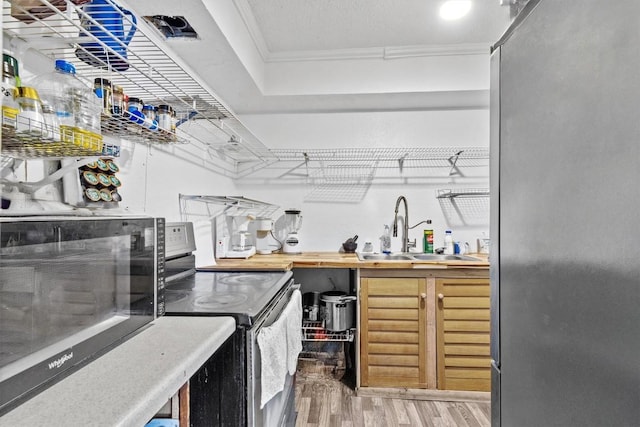 bar featuring electric range oven, ornamental molding, freestanding refrigerator, a sink, and light wood-type flooring