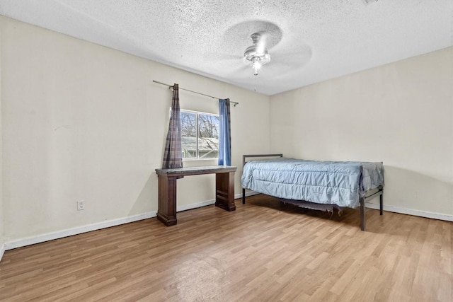 bedroom with a ceiling fan, a textured ceiling, baseboards, and wood finished floors