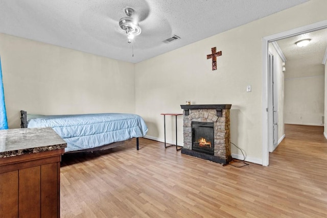 bedroom with a textured ceiling, light wood-style flooring, a fireplace, and visible vents