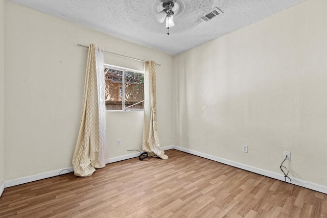 unfurnished room with a textured ceiling, wood finished floors, a ceiling fan, visible vents, and baseboards