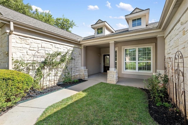 doorway to property featuring stone siding, roof with shingles, a lawn, and stucco siding