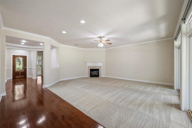 unfurnished living room with recessed lighting, wood finished floors, baseboards, a glass covered fireplace, and crown molding