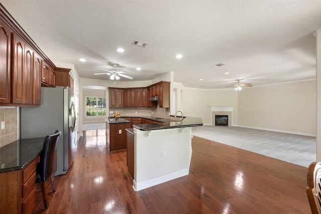 kitchen with visible vents, dark wood finished floors, a glass covered fireplace, ceiling fan, and a peninsula