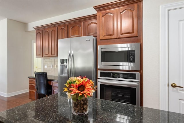 kitchen featuring dark stone counters, stainless steel appliances, decorative backsplash, and wood finished floors