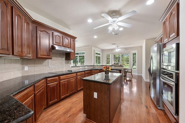 kitchen with under cabinet range hood, a peninsula, a sink, appliances with stainless steel finishes, and backsplash