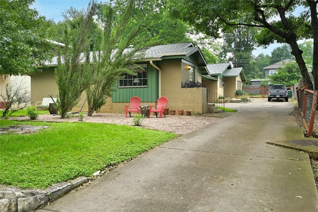 view of front facade with brick siding, fence, driveway, roof with shingles, and board and batten siding