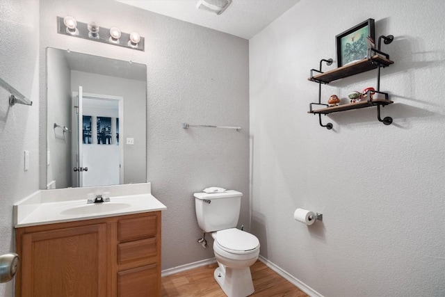 half bath with visible vents, toilet, vanity, wood finished floors, and baseboards