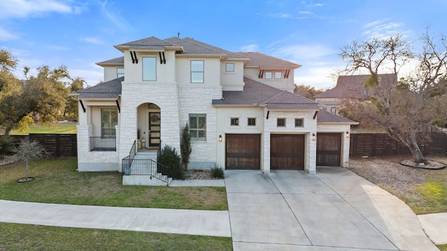 view of front of property with driveway, stone siding, an attached garage, fence, and a front yard