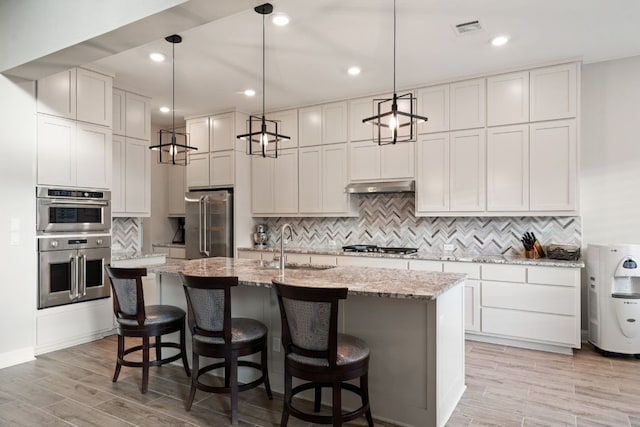 kitchen with light wood finished floors, visible vents, appliances with stainless steel finishes, under cabinet range hood, and a sink