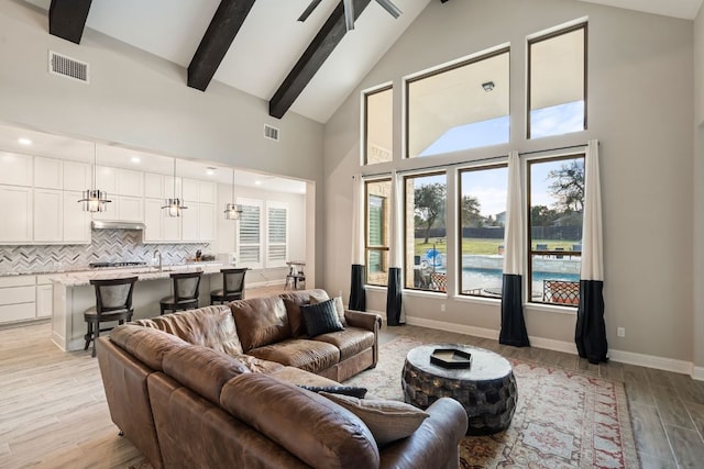 living area with high vaulted ceiling, light wood-style flooring, visible vents, and beam ceiling