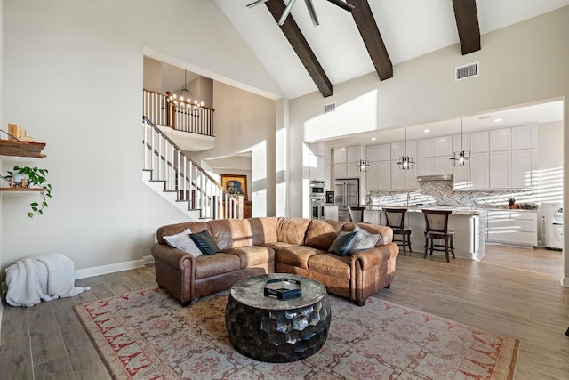 living room with light wood-style floors, stairway, visible vents, and beam ceiling