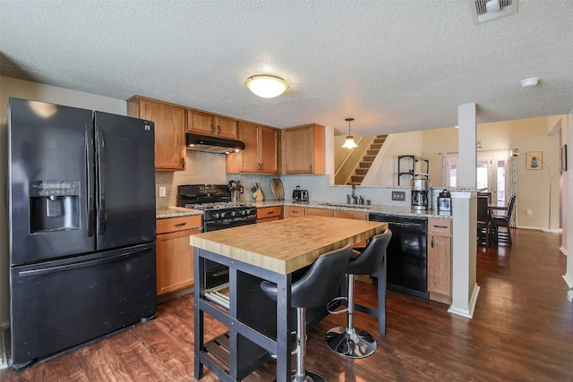 kitchen featuring black appliances, under cabinet range hood, a peninsula, dark wood-style flooring, and decorative backsplash