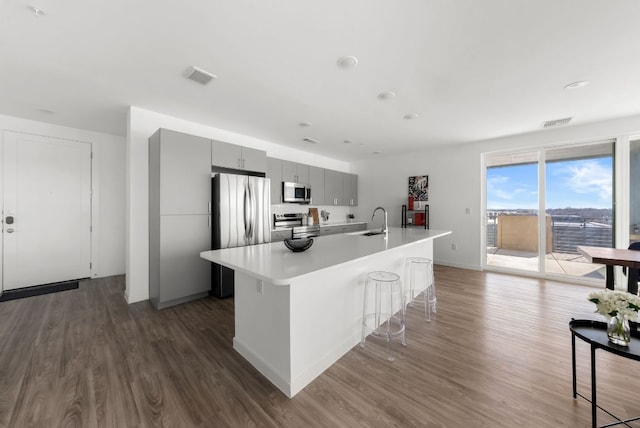 kitchen with visible vents, a breakfast bar, stainless steel appliances, gray cabinets, and a sink