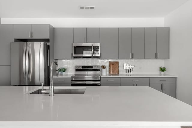 kitchen with stainless steel appliances, visible vents, a sink, and gray cabinetry