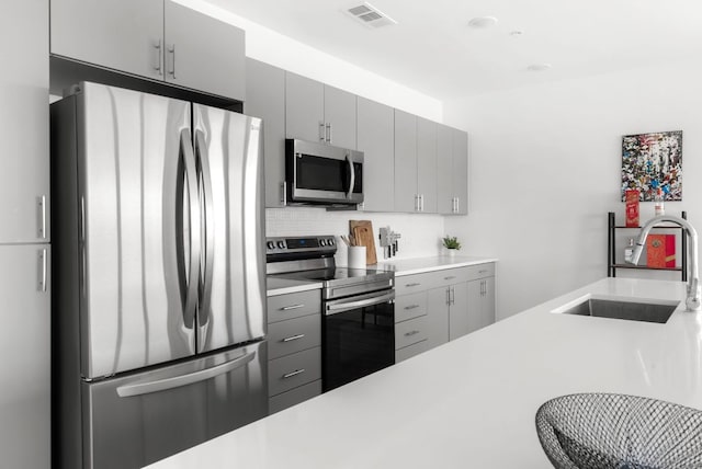 kitchen featuring stainless steel appliances, gray cabinets, visible vents, decorative backsplash, and a sink