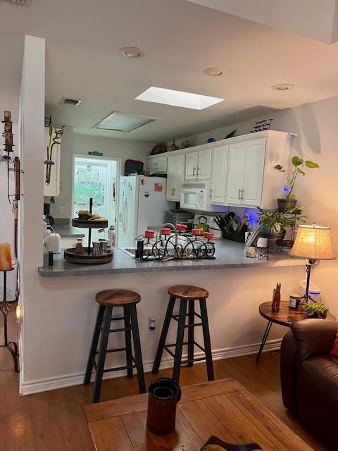 kitchen featuring a skylight, white appliances, a peninsula, and wood finished floors