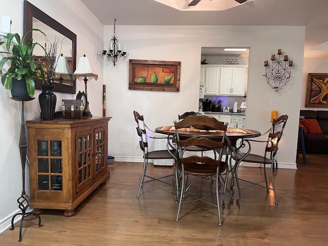 dining area featuring ceiling fan with notable chandelier, baseboards, and wood finished floors