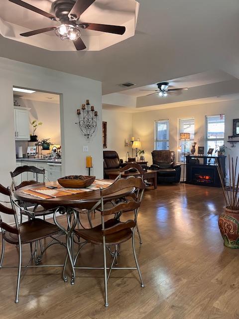 dining room featuring visible vents, a tray ceiling, wood finished floors, and a ceiling fan