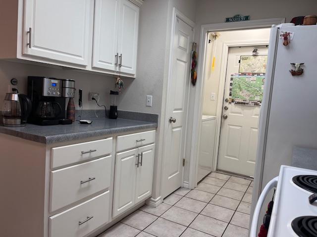 kitchen featuring light tile patterned floors, white appliances, dark countertops, and white cabinetry