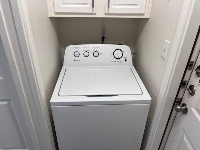 clothes washing area with cabinet space, washer / clothes dryer, and a textured wall