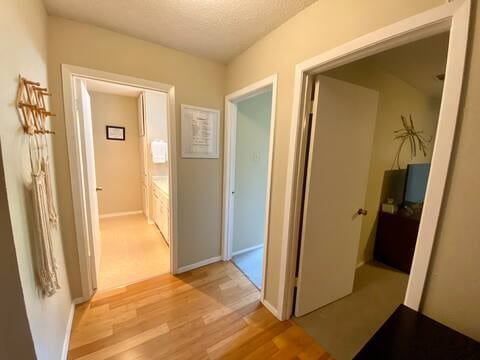 hall featuring a textured ceiling, light wood-type flooring, and baseboards