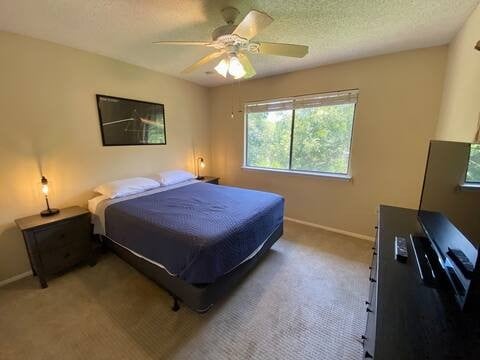 bedroom with ceiling fan, baseboards, a textured ceiling, and light colored carpet