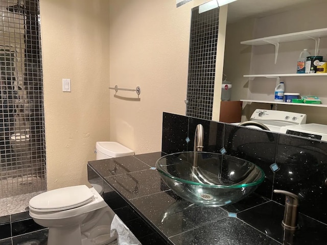 bathroom with washer / dryer, tiled shower, toilet, tile patterned floors, and a sink