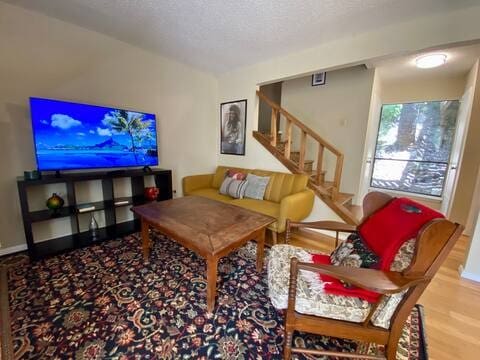 living area with a textured ceiling, stairway, wood finished floors, and baseboards