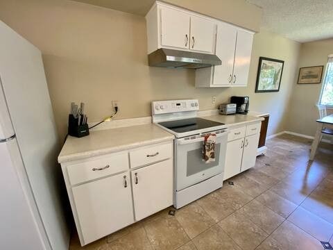 kitchen featuring a textured ceiling, under cabinet range hood, white appliances, white cabinets, and light countertops