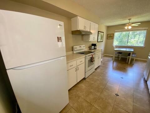 kitchen with white appliances, white cabinets, light countertops, a textured ceiling, and under cabinet range hood