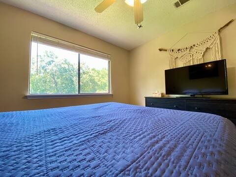 bedroom with ceiling fan, visible vents, vaulted ceiling, and a textured ceiling