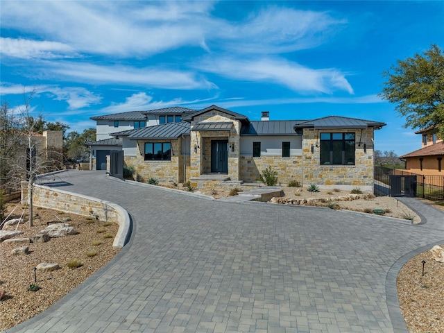 2923 Cliff Pt, Spicewood, TX 78669 - modern home featuring a standing seam roof, decorative driveway, metal roof, stone siding, and a gate
