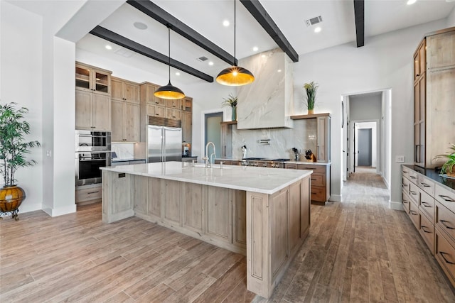 2923 Cliff Pt, Spicewood, TX 78669 - kitchen featuring appliances with stainless steel finishes, beam ceiling, tasteful backsplash, light wood-style flooring, and a large island with sink
