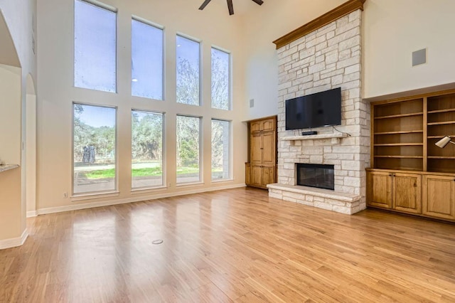 unfurnished living room featuring a high ceiling, a fireplace, wood finished floors, and a ceiling fan