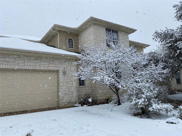 snow covered property with a garage and stone siding