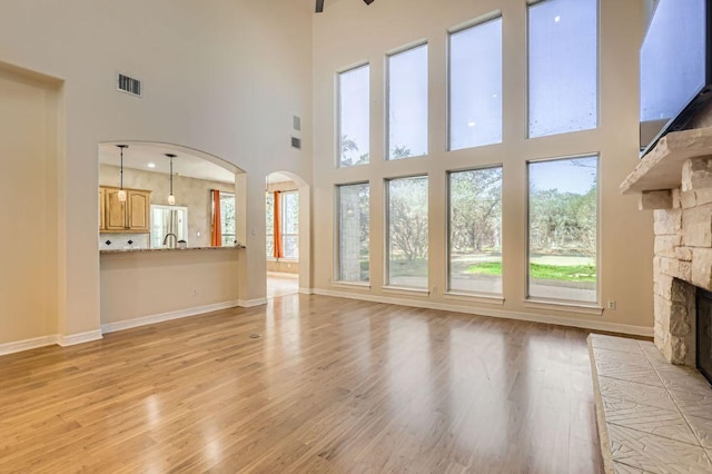 unfurnished living room with light wood-style flooring, visible vents, a stone fireplace, and baseboards