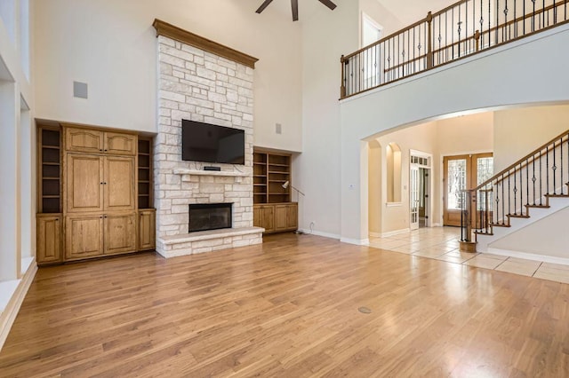 unfurnished living room with a ceiling fan, a stone fireplace, light wood-type flooring, baseboards, and stairs