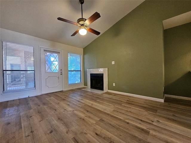 unfurnished living room featuring high vaulted ceiling, wood finished floors, a high end fireplace, baseboards, and a ceiling fan