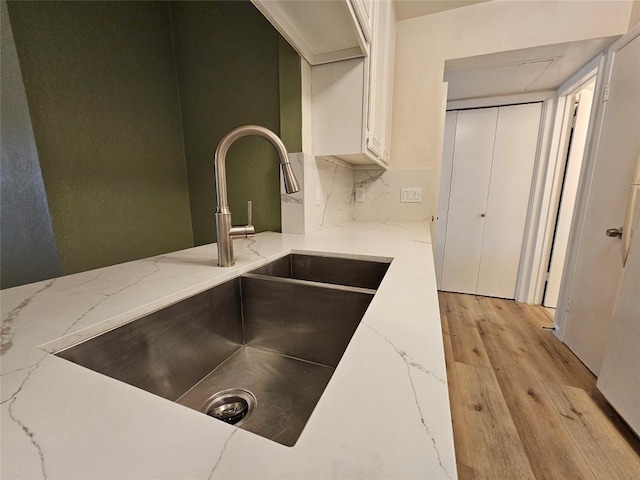 interior details featuring light wood-type flooring, light stone countertops, white cabinetry, and a sink